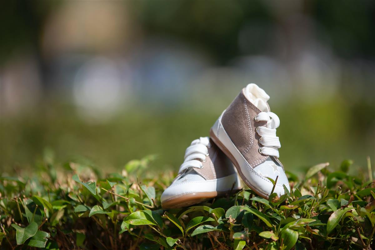 Beige/hvite baby sko som står oppå en grønn hekk.  - Klikk for stort bilde